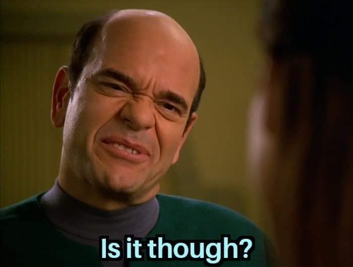 The meme features a still image of the character Holographic Doctor from the TV show "Star Trek: The Next Generation" with a puzzled expression. The text "Is it though?" appears below the image, implying that the character's confused face is responding to a statement or question with a sarcastic or ironic tone. The meme is likely used to express skepticism or incredulity in response to a situation or statement.